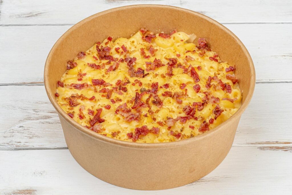 A casserole dish of vegan macaroni and cheese with a browned topping and serving spoon.