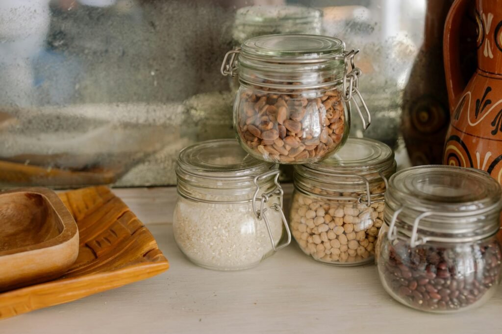 An organized pantry shelf with jars of beans, rice, spices, canned tomatoes, and vinegar.