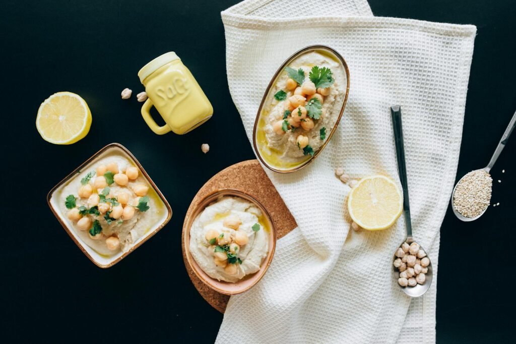 A blender jar filled with creamy vegan sauce next to lemon halves and garlic on a kitchen counter