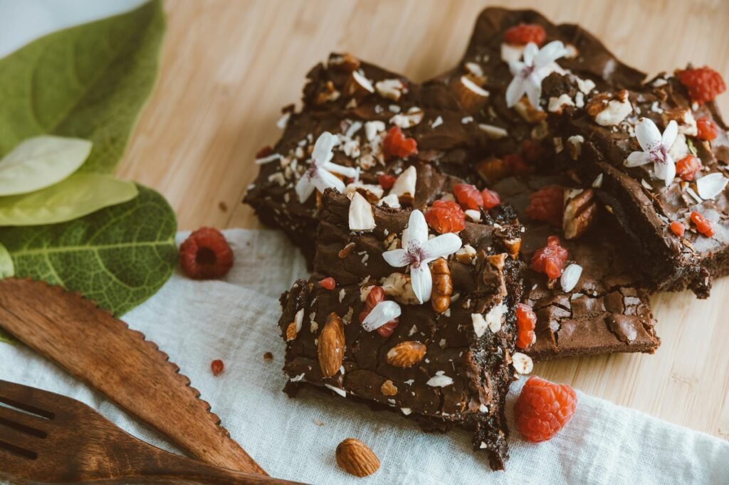 Brownie squares cooling on parchment paper beside cocoa powder and oil