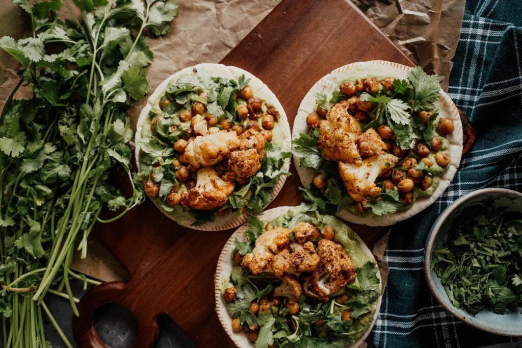 Roasted cauliflower, chickpeas, and red onion on a sheet pan with lemon wedges and chopped herbs.