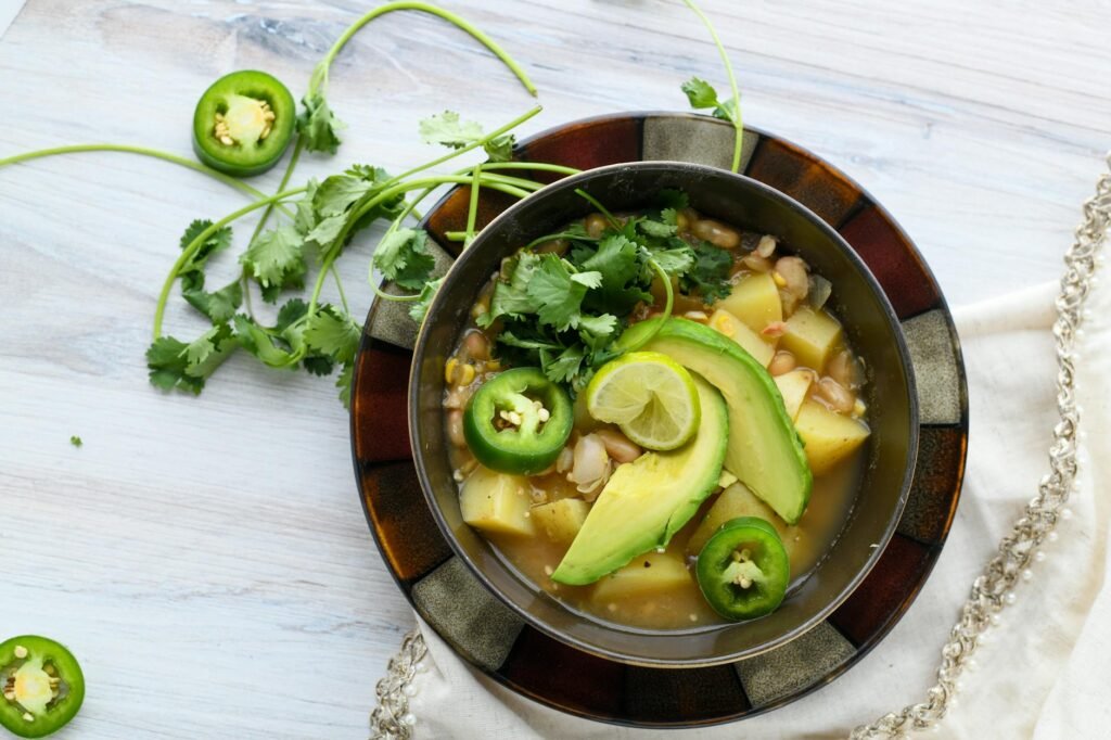 A pot of black bean and sweet potato chili with lime wedges and pumpkin seeds nearby.