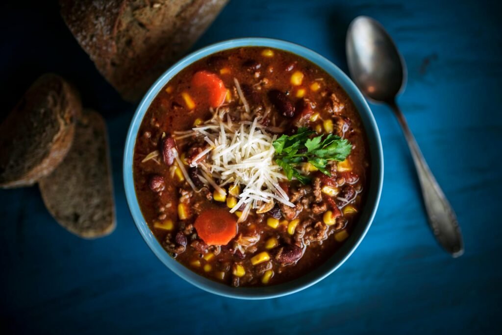 A pot of chili with baked potatoes, scallions, cilantro, and tortilla chips on a kitchen counter.