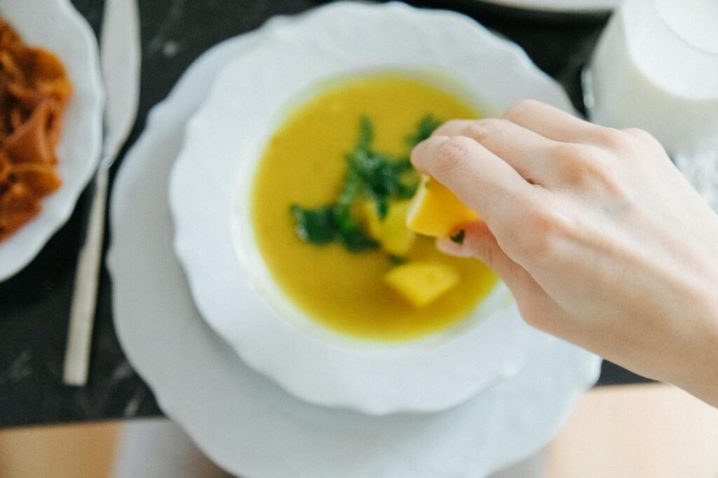 A cook tasting soup with nearby bowls of lemon juice, salt, and nutritional yeast.