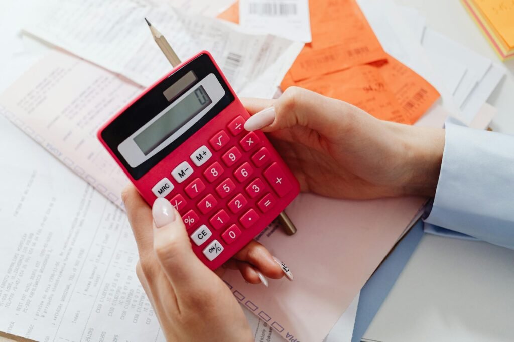 A notebook, grocery receipt, and calculator on a kitchen table beside pantry ingredients.
