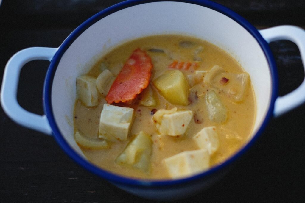 An immersion blender pureeing a pot of vegan soup on the stove.